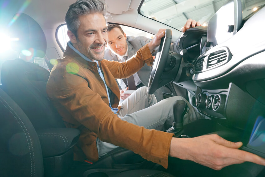 Grey-haired man sitting inside vehicle in car dealership