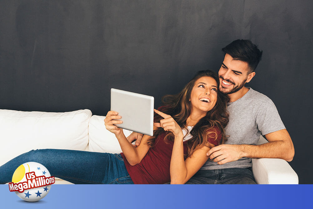 Couple sitting on sofa smiling with the woman pointing at computer screen