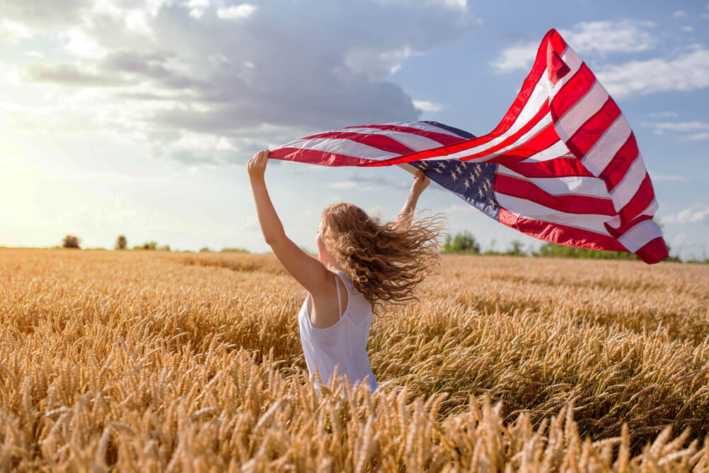 Junge Frau rennt durch ein Kornfeld mit einer amerikanischen Flagge