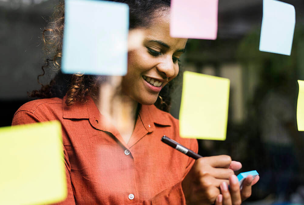 Frau macht sich lächelnd Notizen auf bunten Post-its