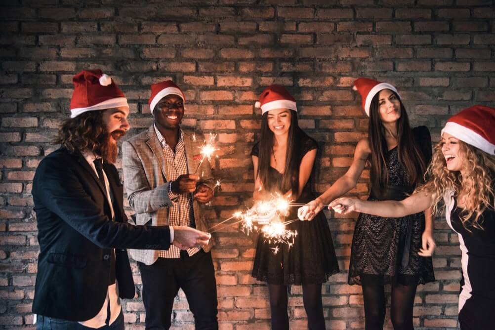 Eine Gruppe von Freunden feiert mit Weihnachtsmützen und Wunderkerzen