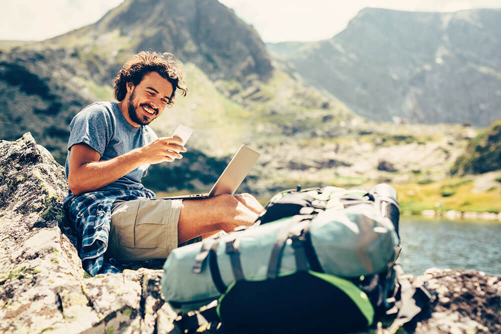 Ein Mann lächelt während er als digitaler Nomade in einer wunderschönen Bergumgebung arbeitet