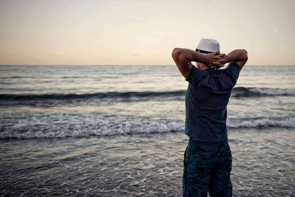 Mann steht am Strand und verschränkt die Arme hinter dem Kopf