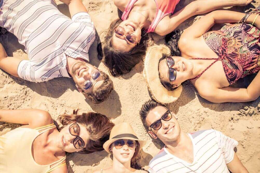 Sechs Freunde liegen lachend im Sand