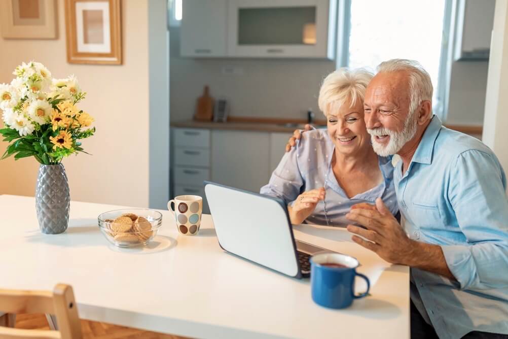 Smiling couple sitting at the kitchen table and looking at the laptop