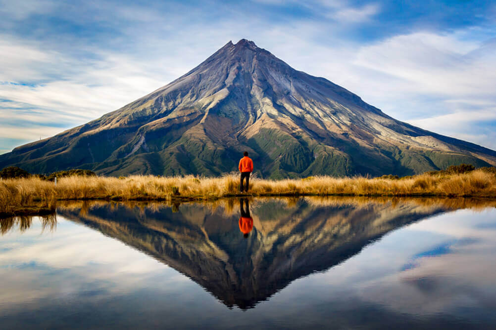 Ein Mann bewundert den Ausblick auf einen Berg, während er sich in einem Bergsee widerspiegelt