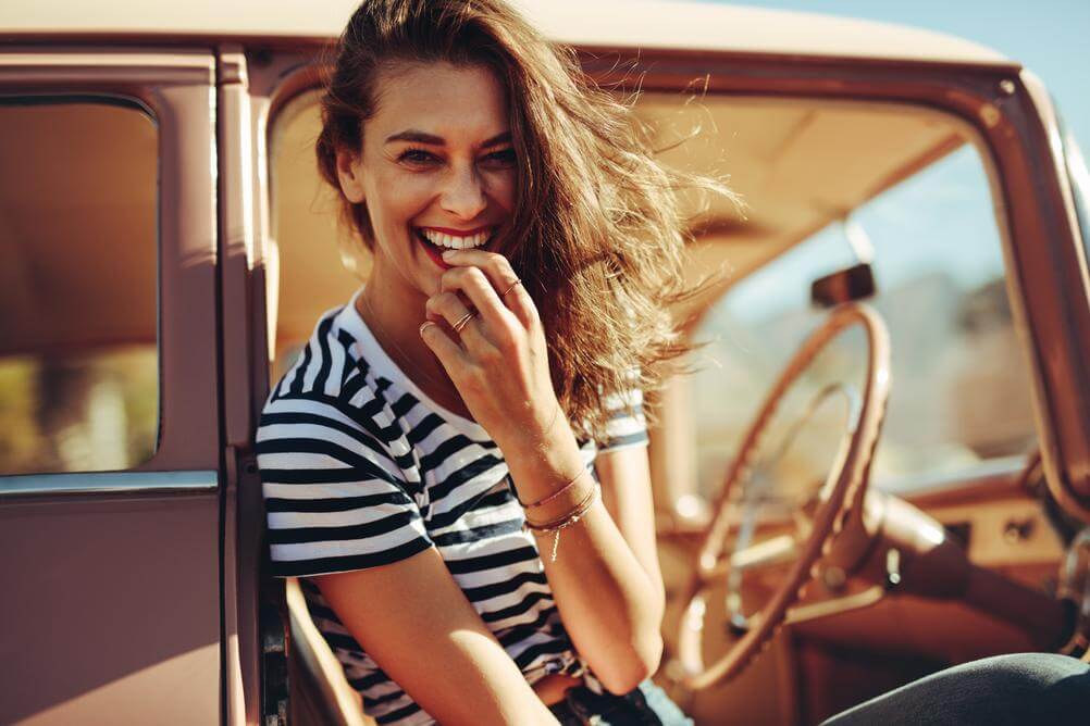 Mulher sentada no carro sorrindo, ao ar livre, celebrando o dia da Mulher