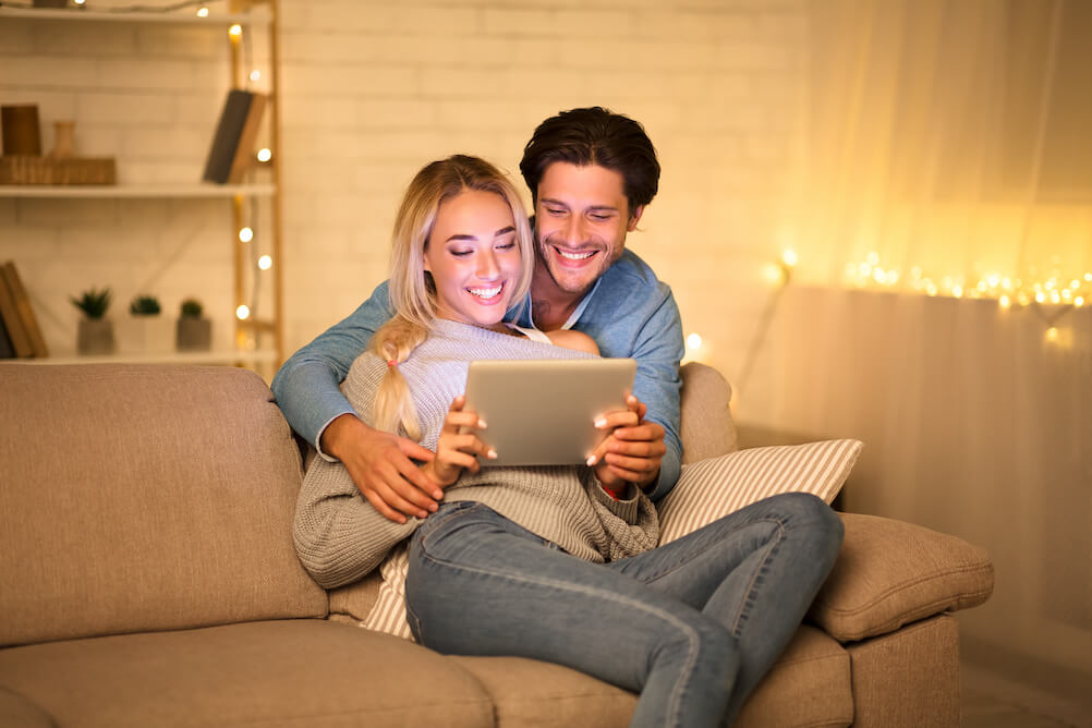 happy-couple-smiling-looking-at-ipad-hugging