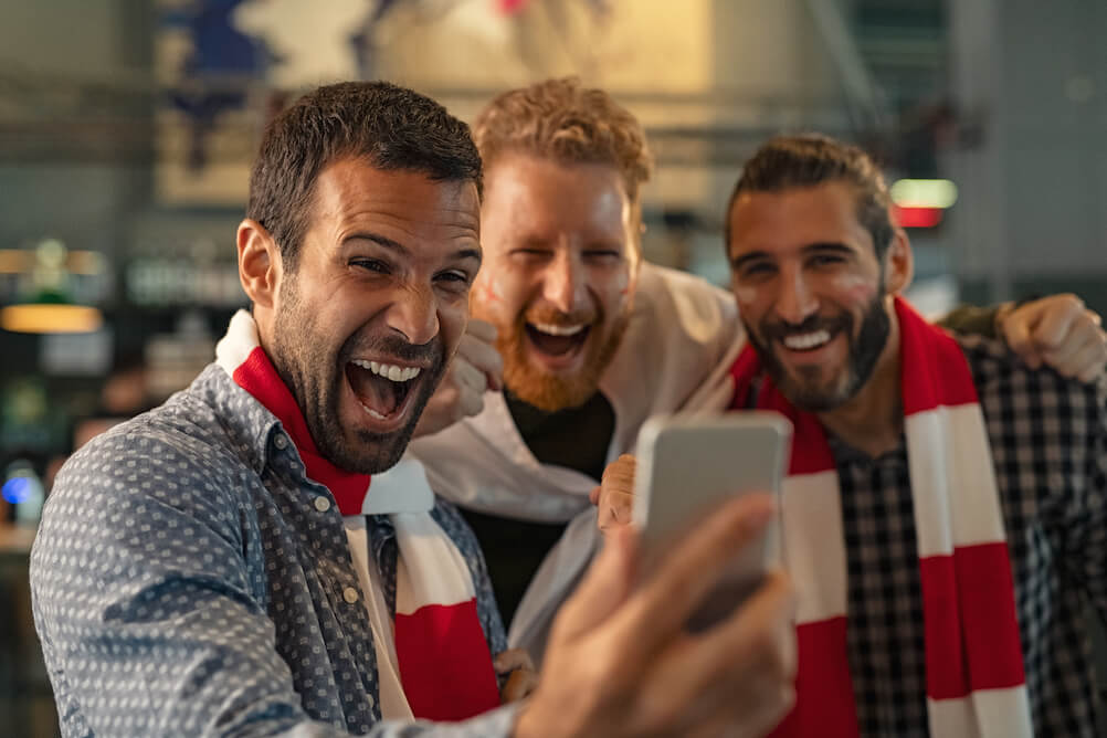Drei lachende Männer mit Schal freuen sich über ihren ersten Sportwetten Gewinn im Lottoland
