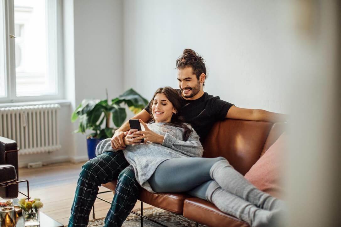 Ein Paar auf einem Sofa in ihrem Wohnzimmer, das die besten Megaways-Slots auf einem Handy genießt.