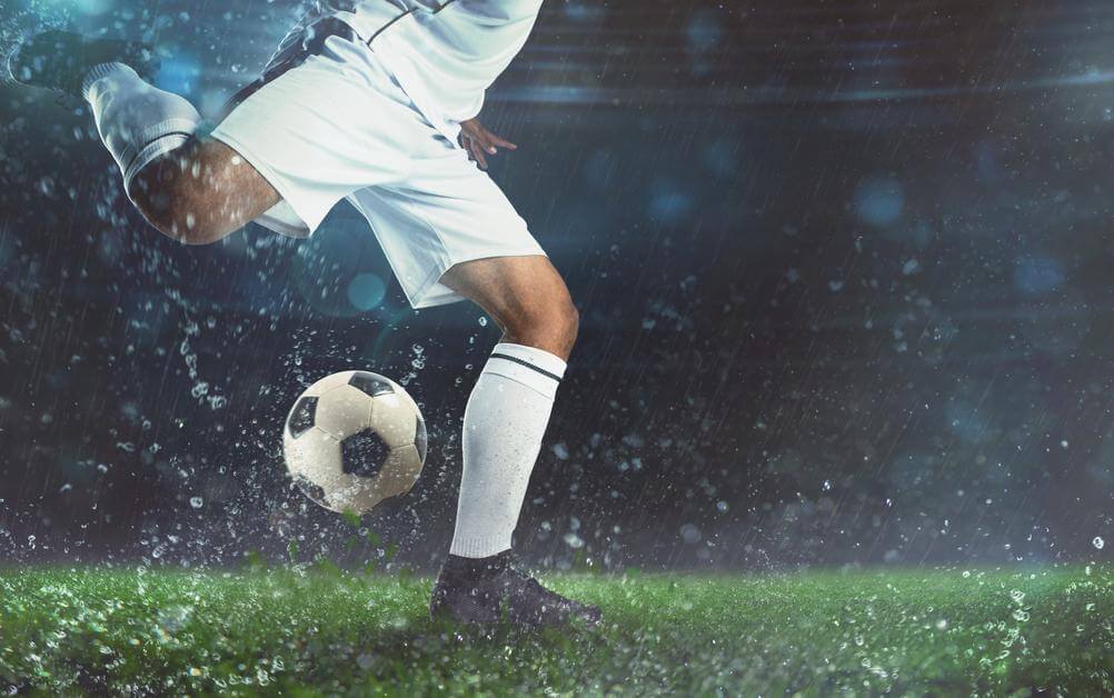 Ein Fußballspieler im weißen Trikot holt zum Schuss aus – ein Sinnbild für die Spannung bei Über/Unter-Wetten.